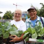 Two people holding armfuls of plants and smiling
