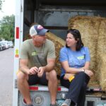 Two people sitting in the back of a truck filled with hay bales