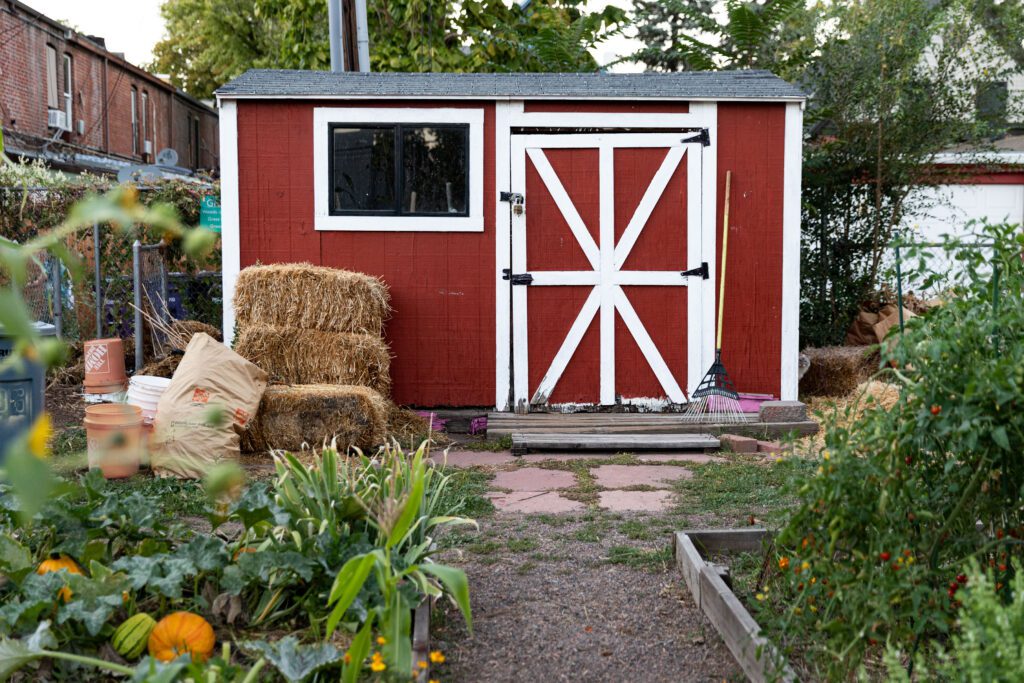 Red barn shed with straw pumpkins and other garden tools - Denver Urban Gardens