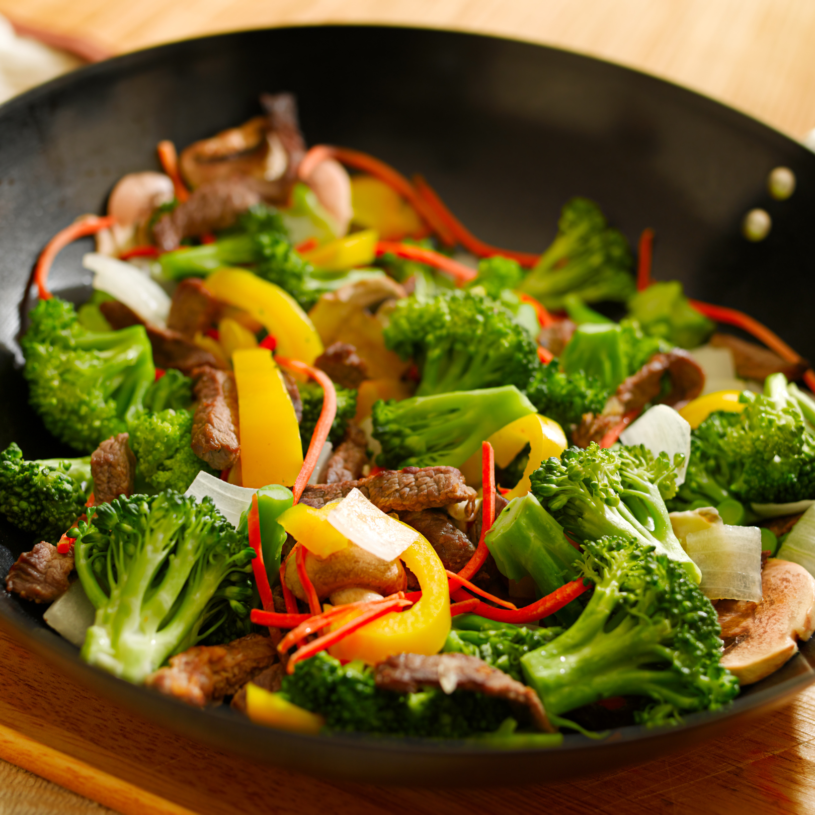 Colorful beef and vegetable stir-fry with broccoli florets, yellow and red bell peppers, and onions in a dark skillet