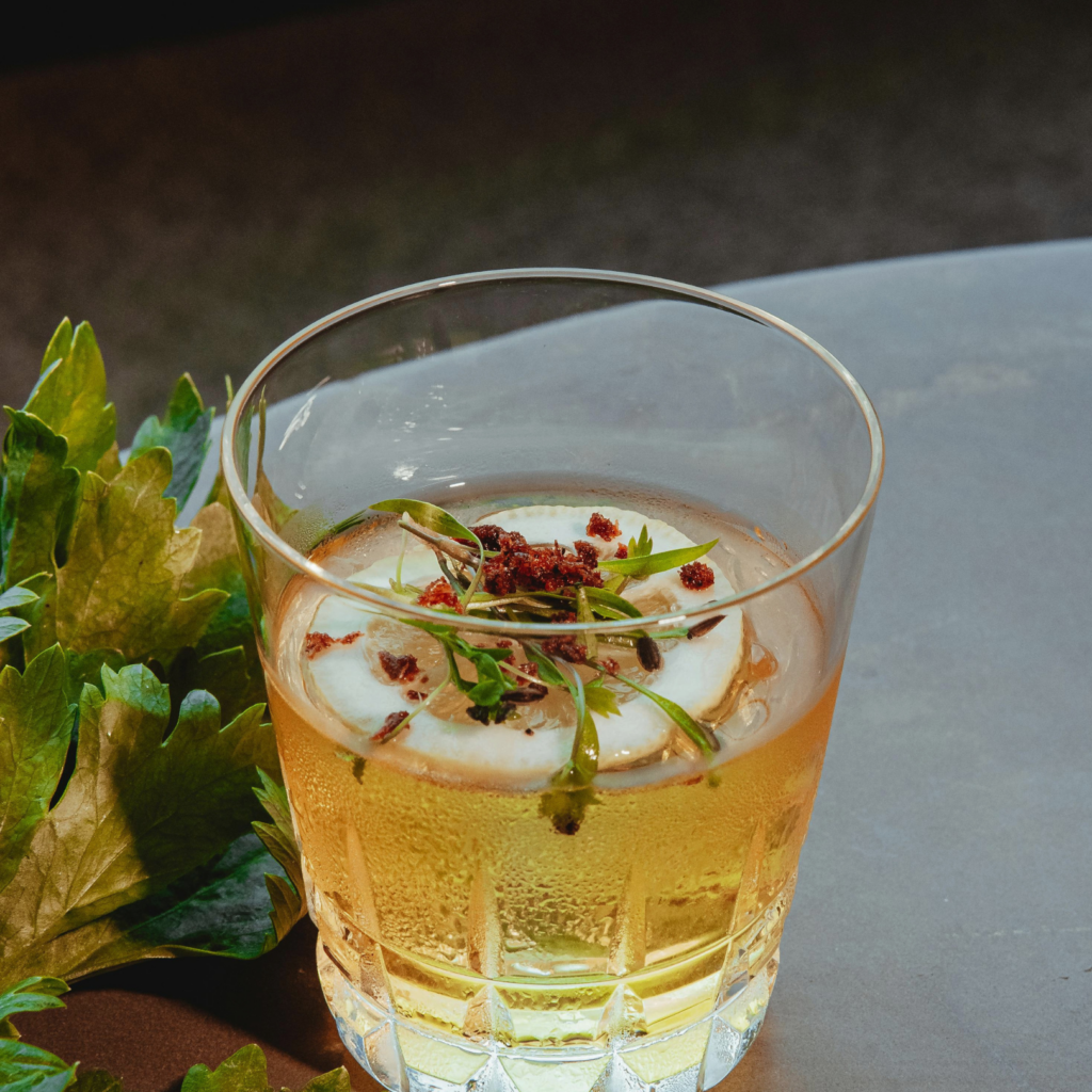 Glass of iced beverage with lemon slice and herb garnish on a textured tabletop.