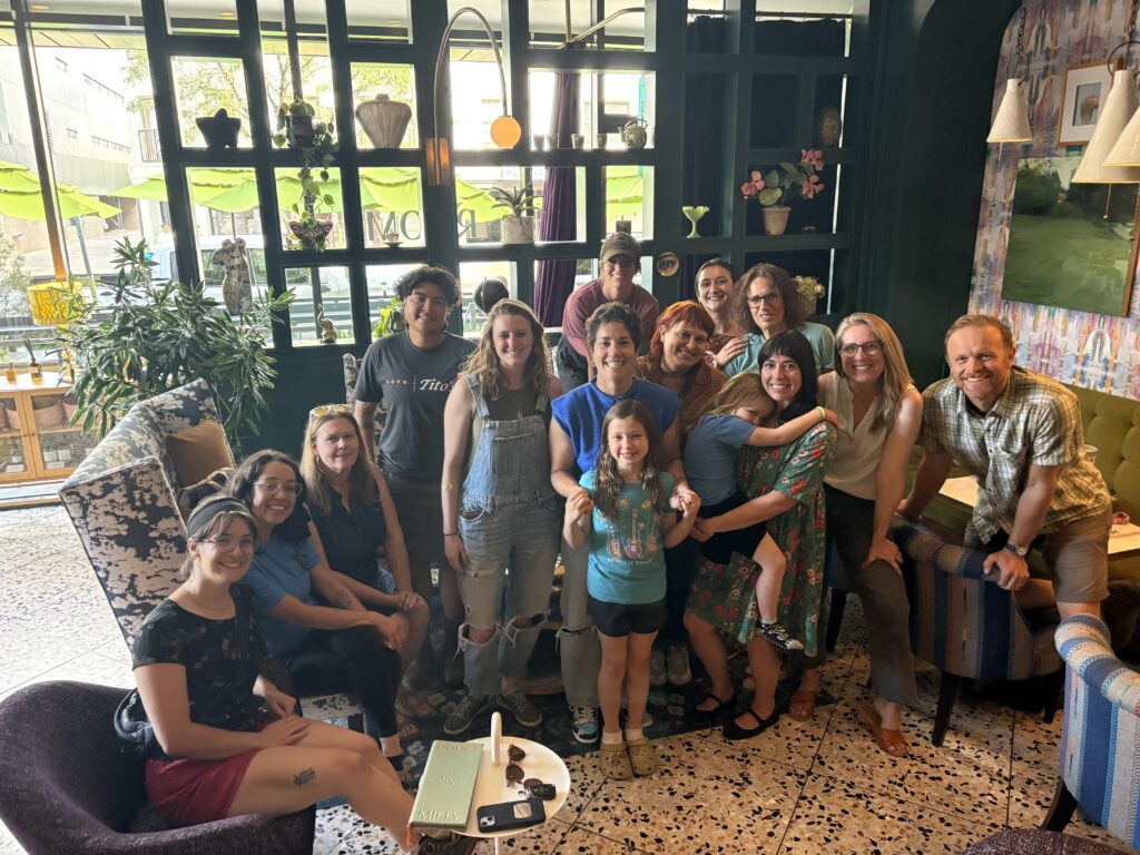 Group of smiling adults and children posing together in a cozy cafe with plants and large windows in the background