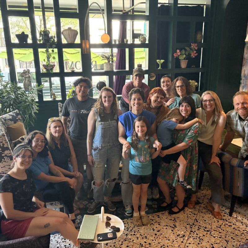 Group of smiling adults and children posing together in a cozy cafe with plants and large windows in the background