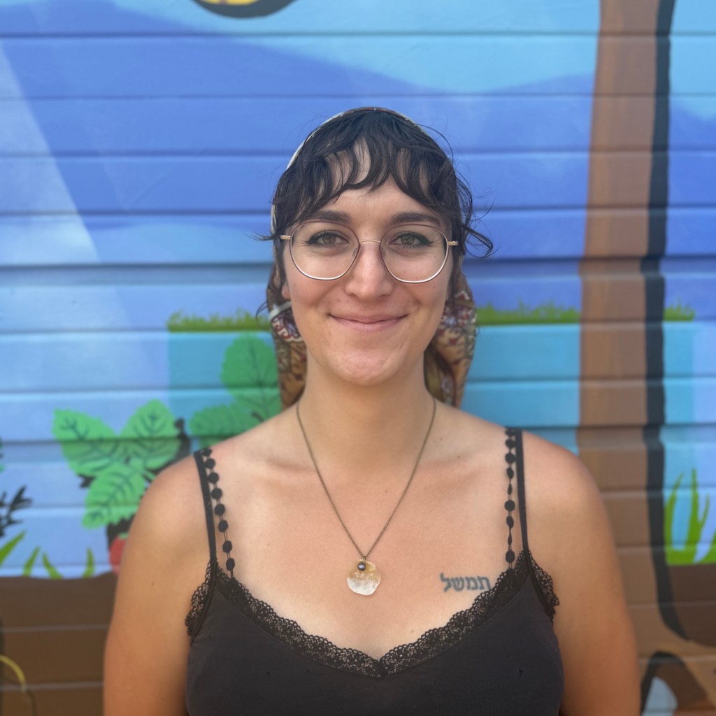 Portrait of a woman with round glasses and a scalloped black top, standing against a blue mural.