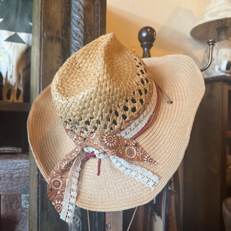 Close-up of a woven straw sun hat with floral ribbon and lace trim on a wooden display.