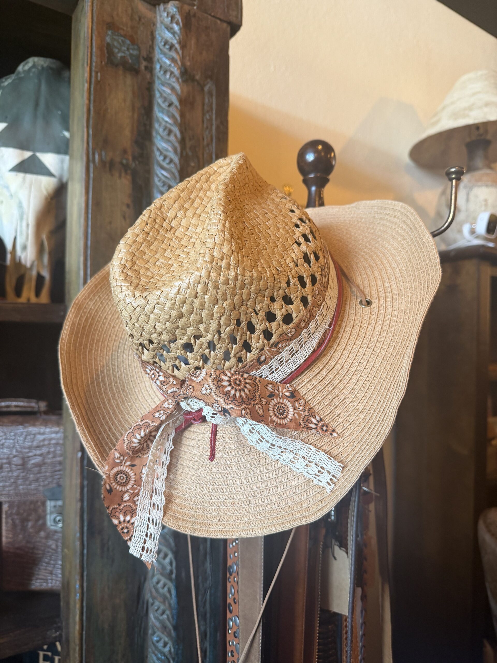 Close-up of a woven straw sun hat with floral ribbon and lace trim on a wooden display.