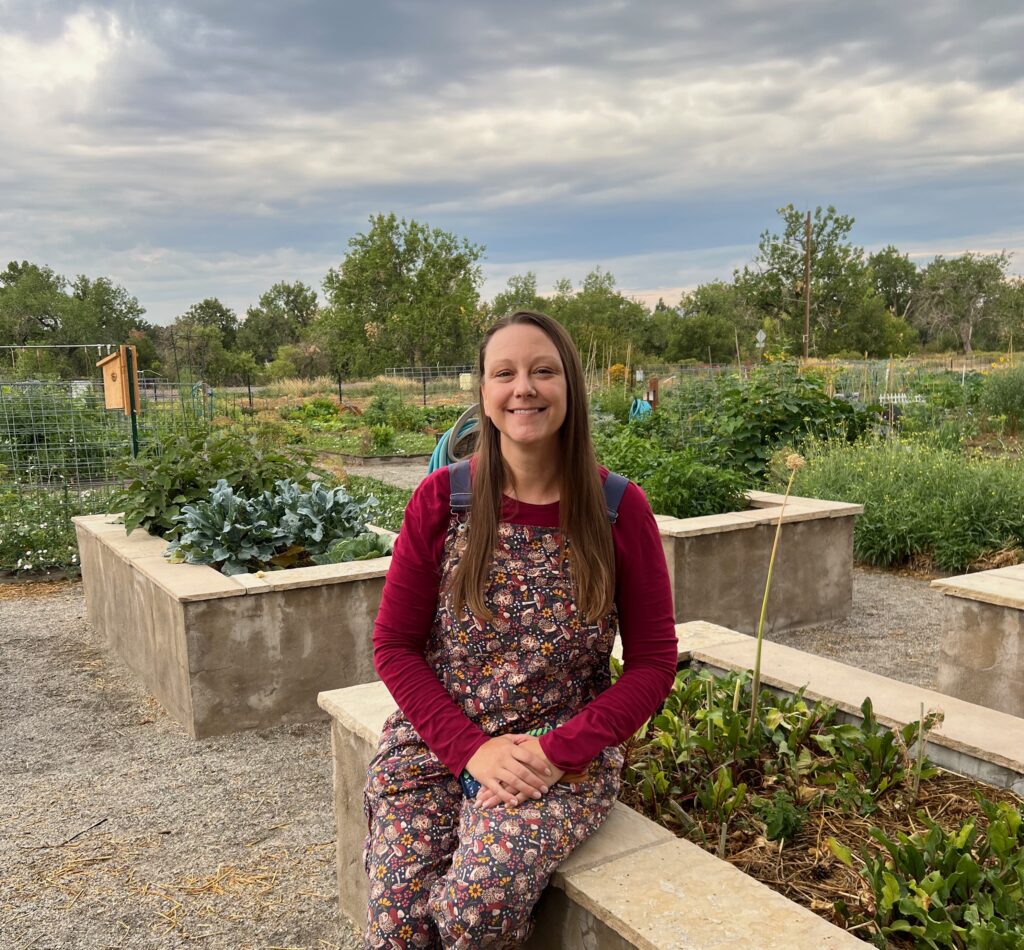 Woman sitting on a stone bench in a garden, wearing a floral dress with maroon sleeves, smiling at the camera.