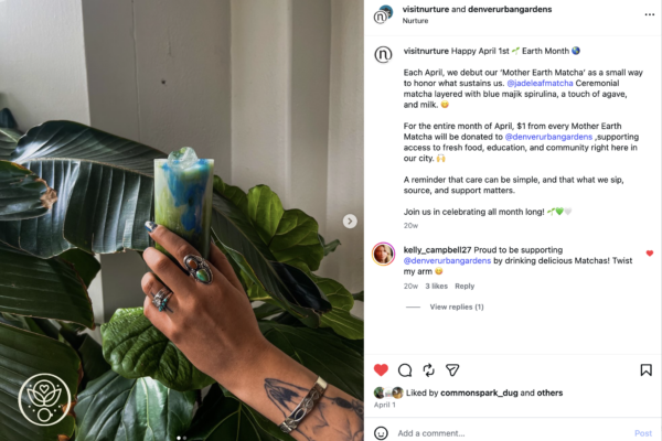 Hand with turquoise rings holding a blue-green layered iced drink among large green leaves.