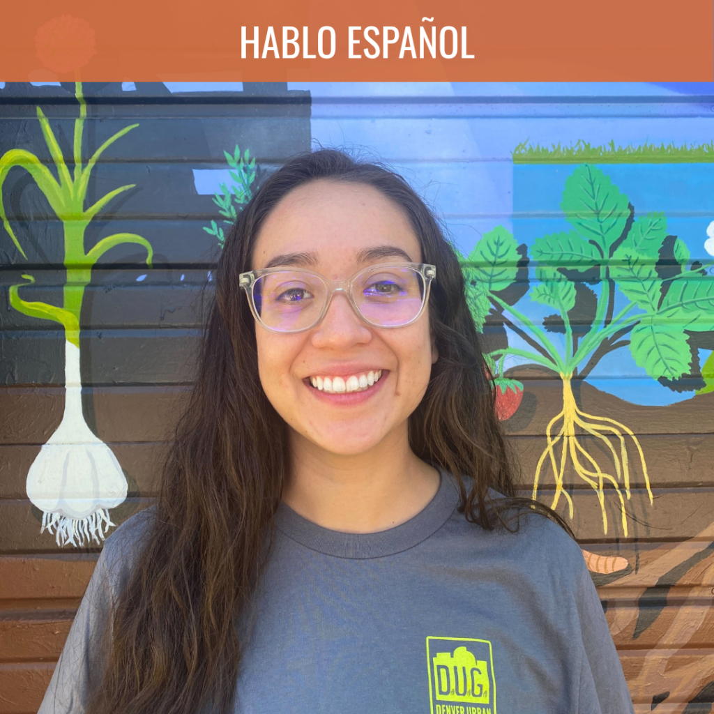 Smiling woman with clear-framed glasses in front of a colorful plant mural behind her.